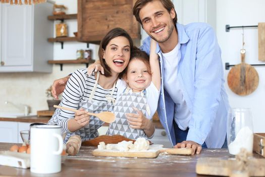 Cute little girl and her parents are having fun while cooking in kitchen at home together