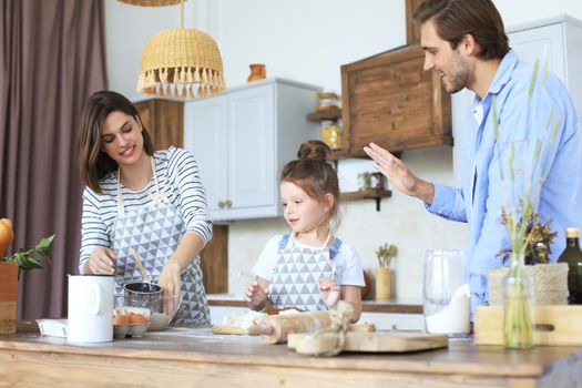 Cute little girl and her parents are having fun while cooking in kitchen at home together