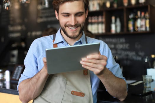 Young male owner using digital tablet while standing in cafe
