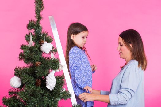 Christmas of young mom and her daughter with Christmas tree on pink background.