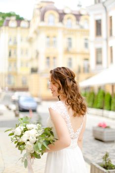 Caucasian fiancee walking with bouquet of flowers in city. Concept of bridal photo session.