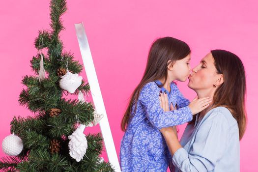 Christmas of young mom and her daughter with Christmas tree on pink background.