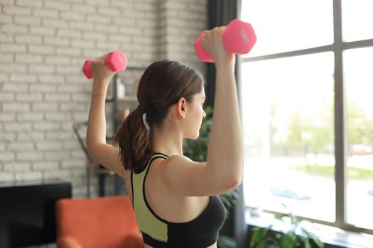 Young beautiful sports girl in leggings and a top does exercises with dumbbells. Healthy lifestyle. A woman goes in for sports at home