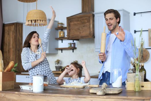 Cute little girl and her parents are having fun while cooking in kitchen at home together