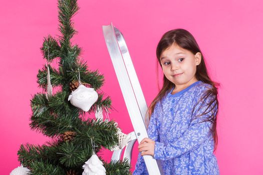 Little girl with christmas tree on pink background.