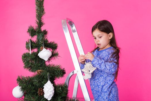 Christmas and holiday concept - A little girl is decorating Christmas tree
