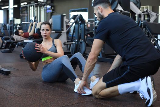 Trainer helping young woman to do abdominal exercises in gym