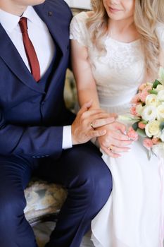 Happy groom wearing suit and red sitting and hugging bride. Concept of wedding photo session and love.