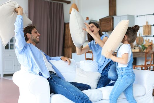 Happy young family having fun with pillows on sofa