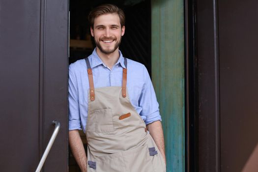 Handsome and confident cafe owner standing at the door. Young man standing with his arms crossed looking at camera smiling