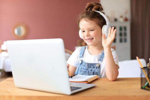 Distance learning. Cheerful little girl girl in headphones using laptop studying through online e-learning system.