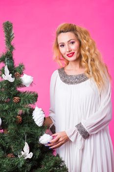 Christmas and holiday concept - Portrait of smiling beautiful blonde woman with Christmas tree on pink background.