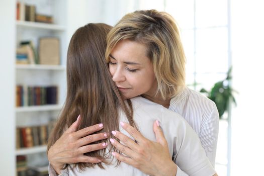 Young woman is embracing her middle aged mother in living room
