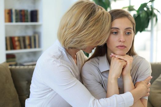 Middle aged mother and daughter talking on sofa in living room