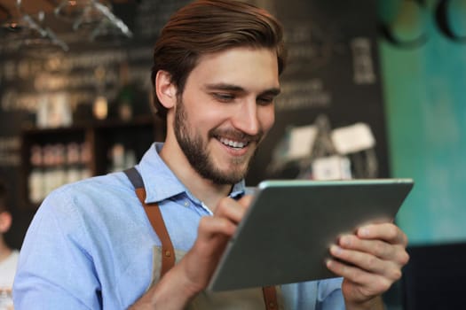 Young male owner using digital tablet while standing in cafe