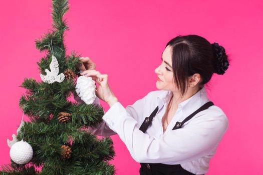Woman near christmas tree on pink background.
