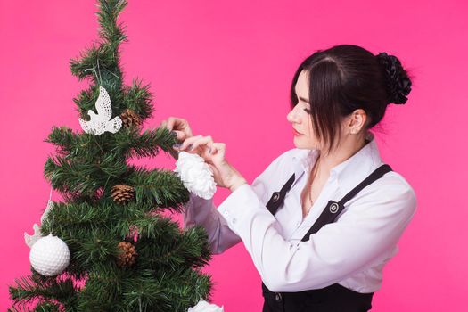 People, holidays and christmas concept - woman decorating christmas tree on pink background.
