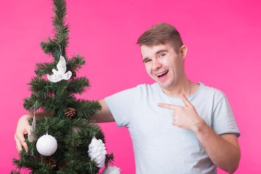 Christmas and holiday concept - Portrait of smiling man with Christmas Tree on pink background.