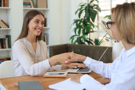 Cheerful female doctor psychologist shaking grateful patient hands after having a consultation meeting