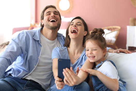 Beautiful young family with little child taking a selfie with a smartphone at home on the couch
