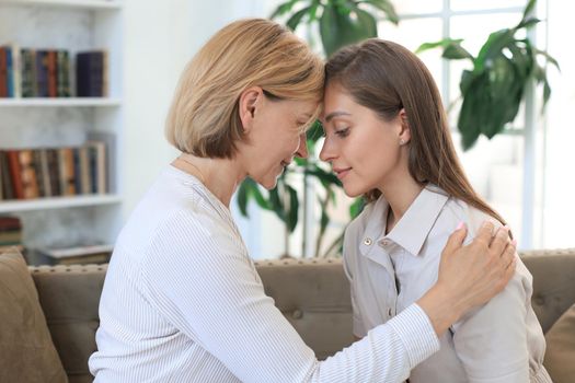 Happy middle aged mother and daughter talking on sofa in living room