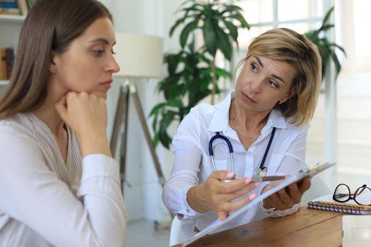 Middle aged female doctor therapist in consultation with patient in office