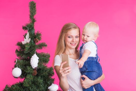 Mother and little daughter taking a selfie near Christmas tree.