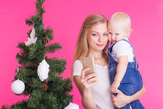 Mother and little daughter taking a selfie near Christmas tree.