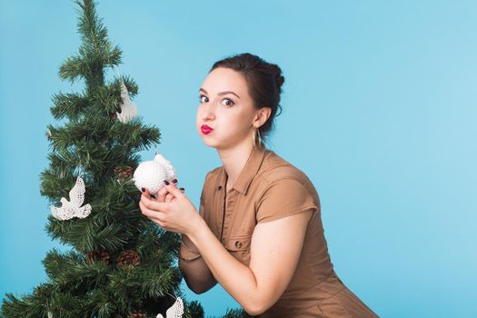 Christmas, holidays and people concept - young happy woman decorating christmas tree on blue background.