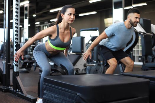Fit couple doing jumping squats in crossfit gym