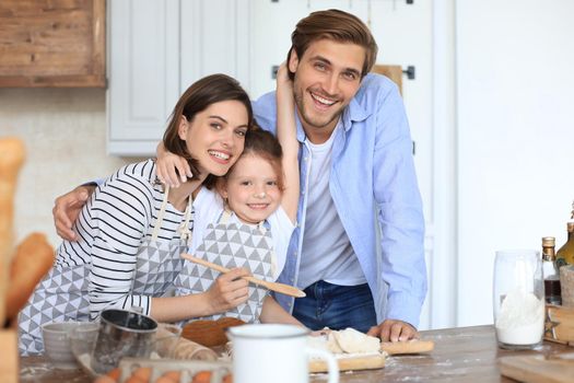 Cute little girl and her parents are having fun while cooking in kitchen at home together