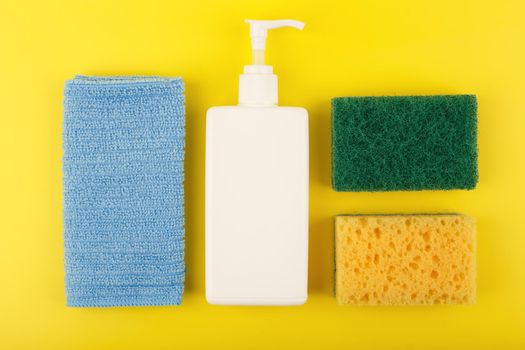 Creative colorful flat lay with detergent in white tube, blue dust cloth and yellow cleaning sponge on saturated yellow background. House cleaning and dishwashing concept