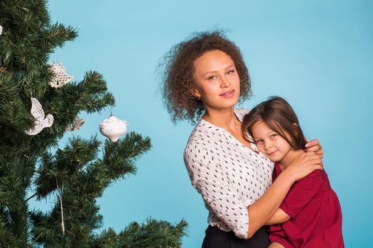 Christmas of young mom and her daughter with Christmas tree on blue background.