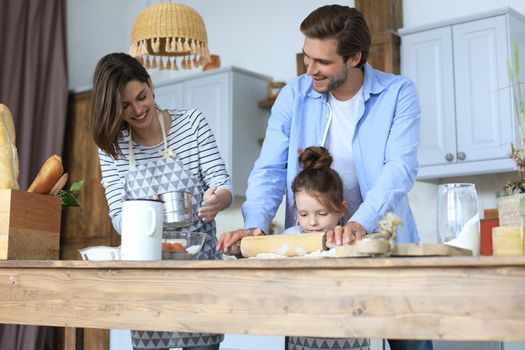 Cute little girl and her parents are having fun while cooking in kitchen at home together