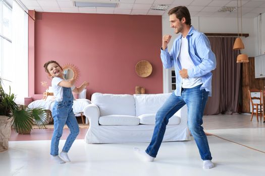 Handsome young man dancing at home with his little cute daugther