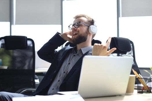 Smiling handsome businessman relaxing and listening music in earphones in a modern office