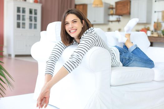 Smiling beautiful woman lying on a sofa in living room at home