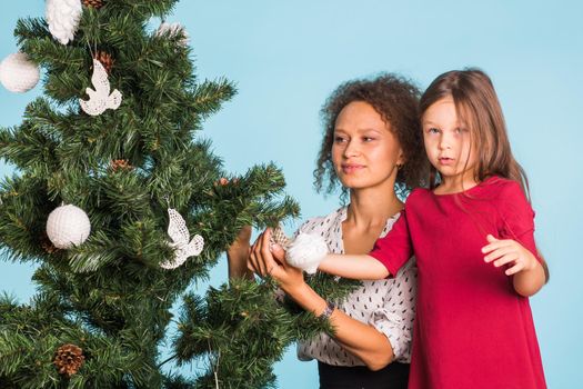 Christmas of young mom and her daughter with Christmas tree on blue background.