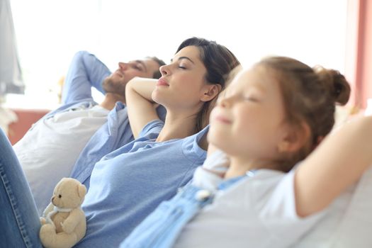 Relaxed young family resting and dreaming about new home on comfortable sofa together at home, happy young parents with little daughter relax enjoying nap relaxing or meditating