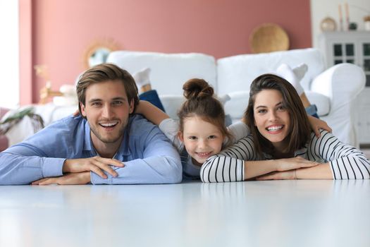 Young Caucasian family with small daughter pose relax on floor in living room, smiling little girl kid hug embrace parents, show love and gratitude, rest at home together
