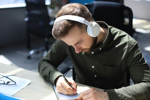 Thoughtful young business man writing something down while working in modern office