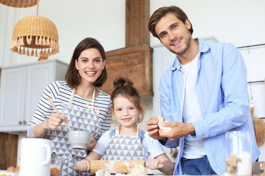 Cute little girl and her parents are having fun while cooking in kitchen at home together