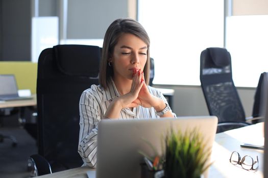 Calm beautiful businesswoman meditating in office with eyes closed