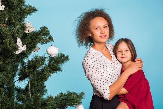 Christmas of young mom and her daughter with Christmas tree on blue background.