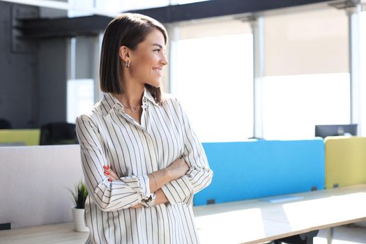 Attractive business woman in smart casual wear looking away and smiling while standing in the office.