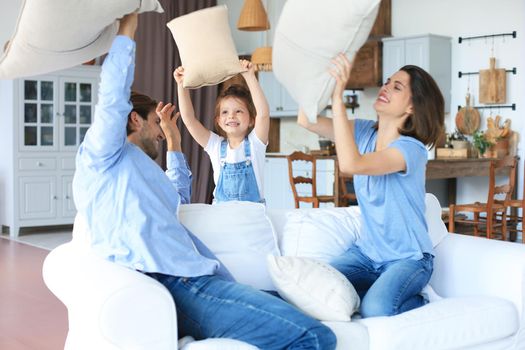 Happy young family having fun with pillows on sofa