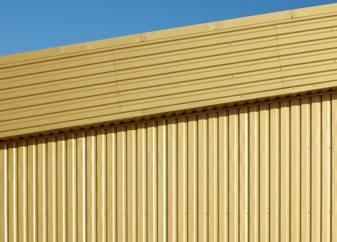Background texture of golden aluminum corrugated goffered metal wall under blue sky