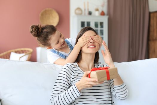 Little girl make birthday present to excited parent , smiling little child congratulate give gift box to happy mother and closed mother's eyes