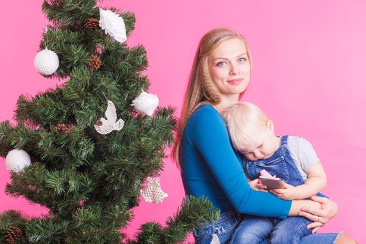 Christmas and holiday concept - Portrait of smiling woman with her little daughter decorating Christmas tree over pink background.