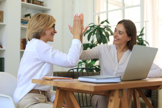 Middle aged businesswoman giving high five to her young female collegue